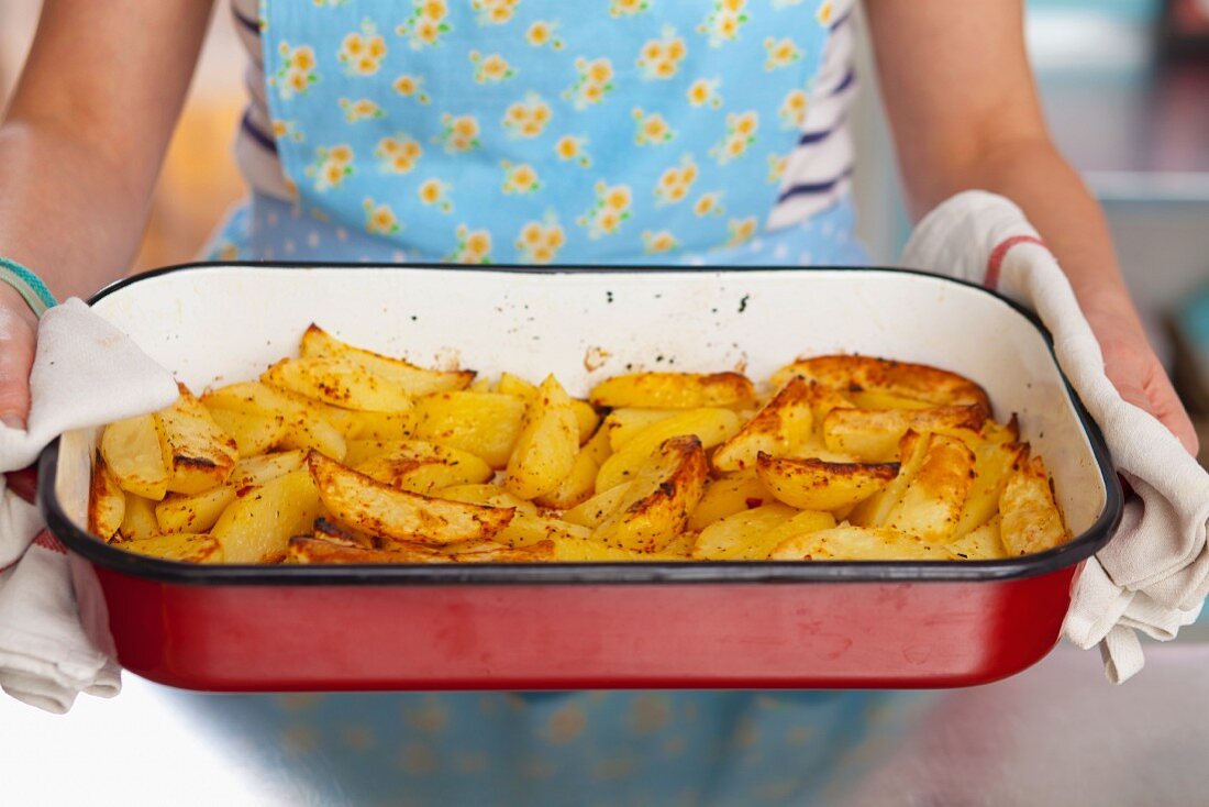 A woman holding a roasting tin full of herb-roasted potatoes