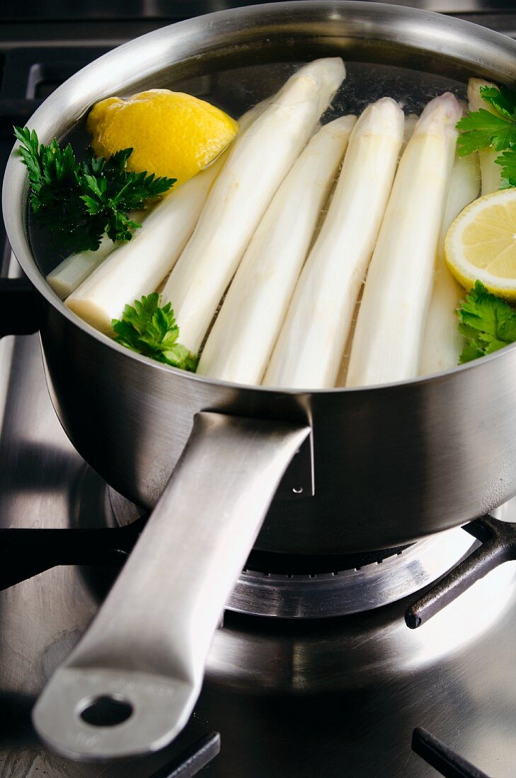 Peeled white asparagus in a saucepan with lemon and parsley