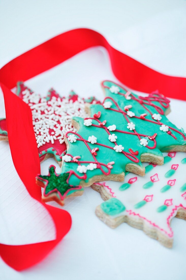 A decorated biscuit in the shape of a Christmas tree, and a red gift ribbon