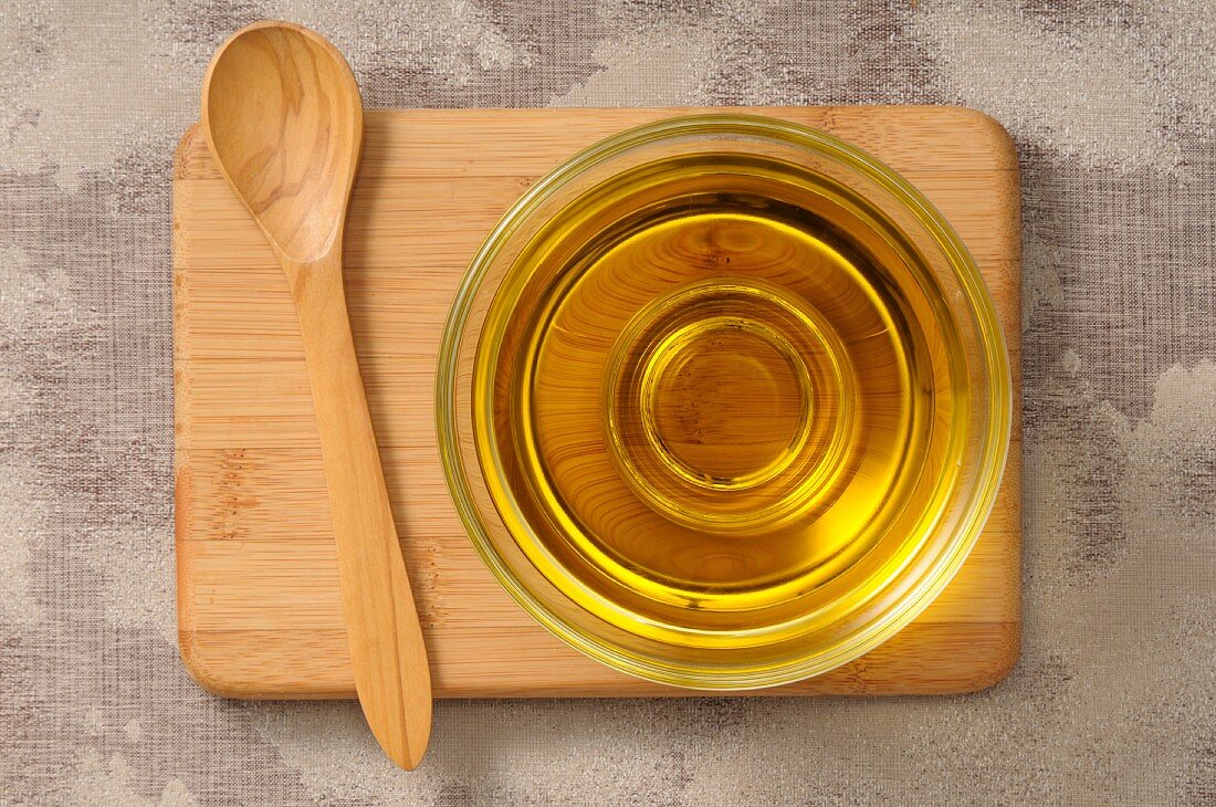 Olive oil in a glass dish on a chopping board with a wooden spoon