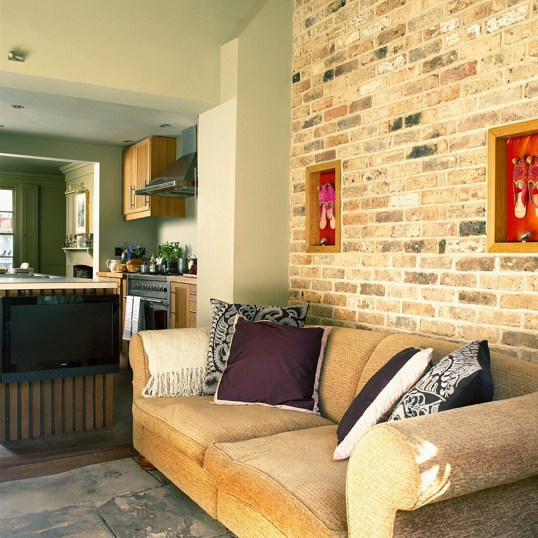 Zimmerflucht in einem Landhaus: Wohnzimmer mit Sofa an einer Ziegelwand, Küche mit Mittelblock und Essecke