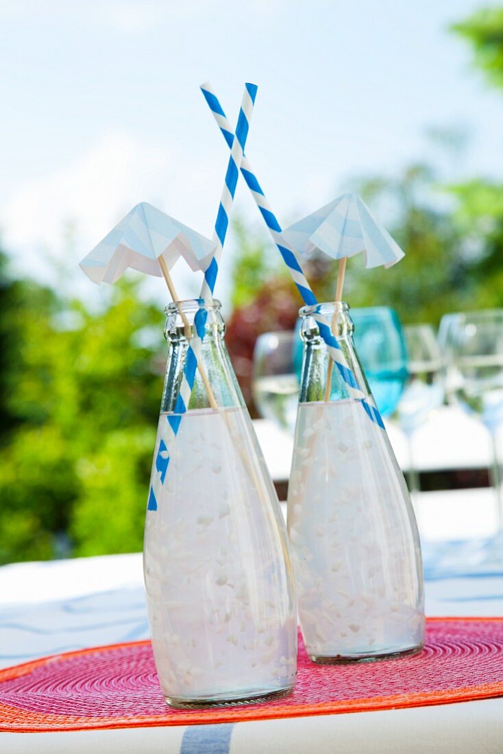 Two bottles with coconut cocktails, straws and paper umbrellas