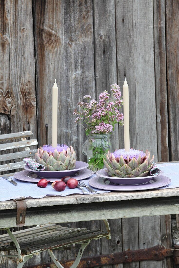 Place settings with candles in artichoke flowers and flowering marjoram in preserving jar
