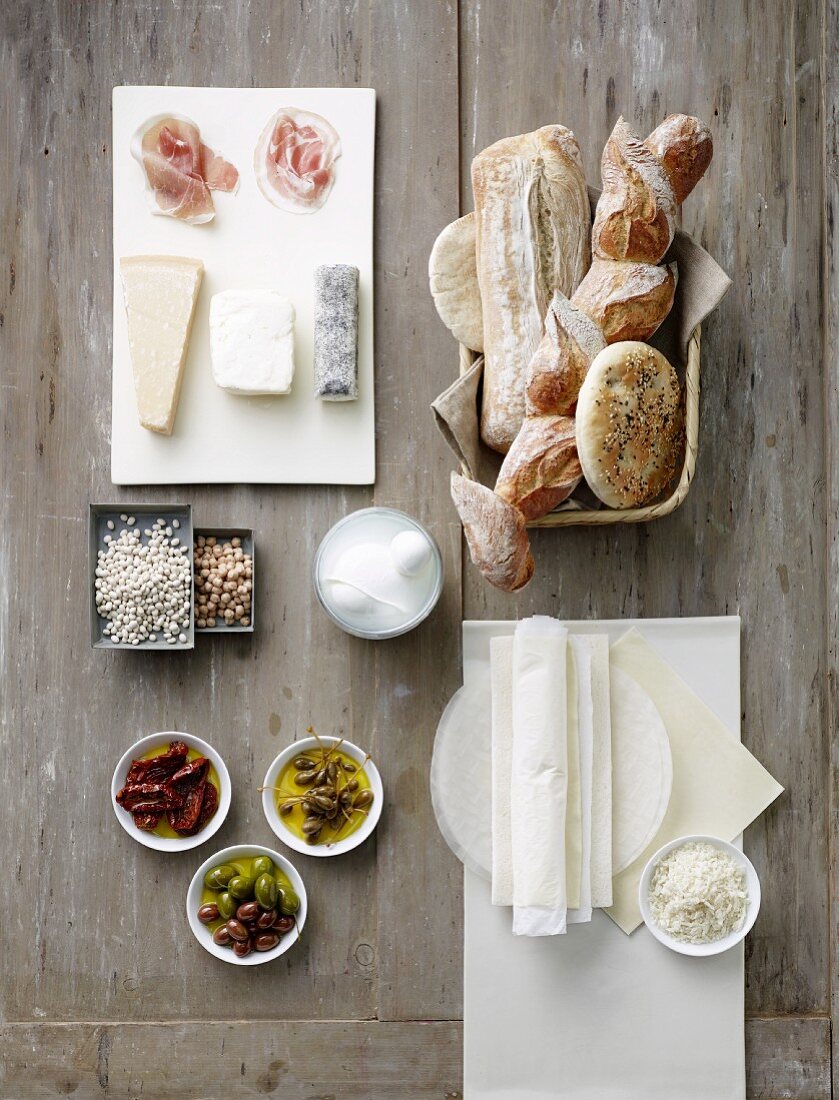 Stillleben mit Brot, Käse, Rohschinken, Oliven, Kapern, getrockneten Tomaten und Reispapier