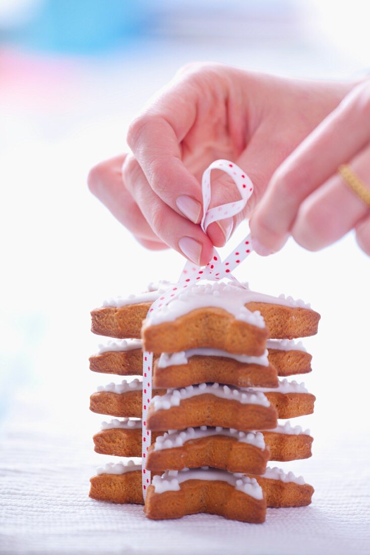 Woman tiding a pile of gingerbread stars garnished with icing