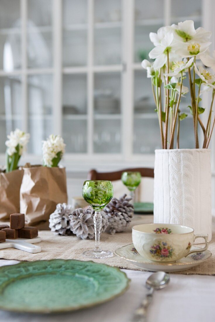 Weihnachtliche Tischdeko mit Hyazinthen und Christrosen in originellen Behältnissen, kombiniert mit Kristallgläser und Blümchentassen