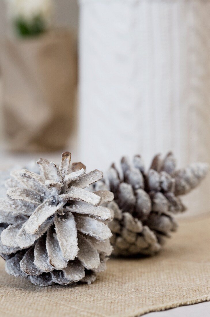 Timeless Christmas table decoration of fir cones sprayed white on ecru linen runner
