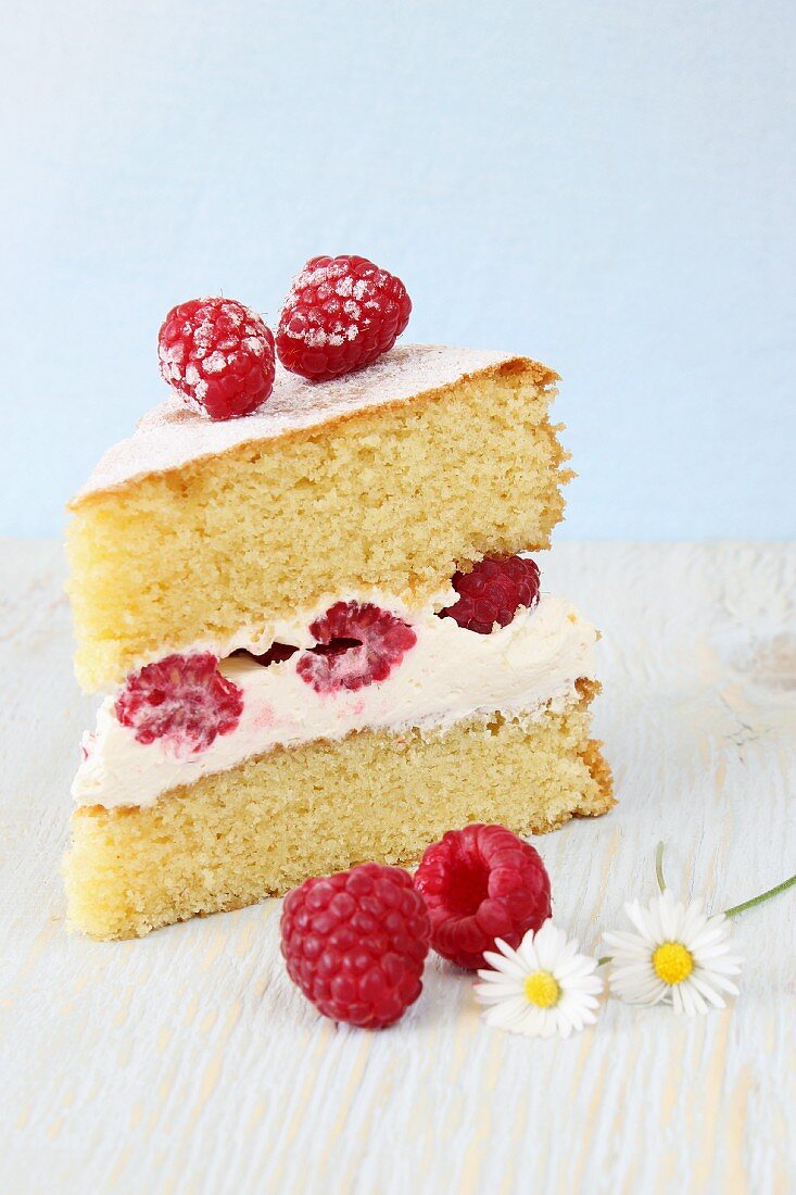 A slice of sponge cake with whipped cream and fresh raspberries
