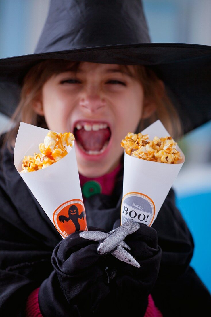 Mädchen hält Papiertüten mit karamellisiertem Popcorn zu Halloween