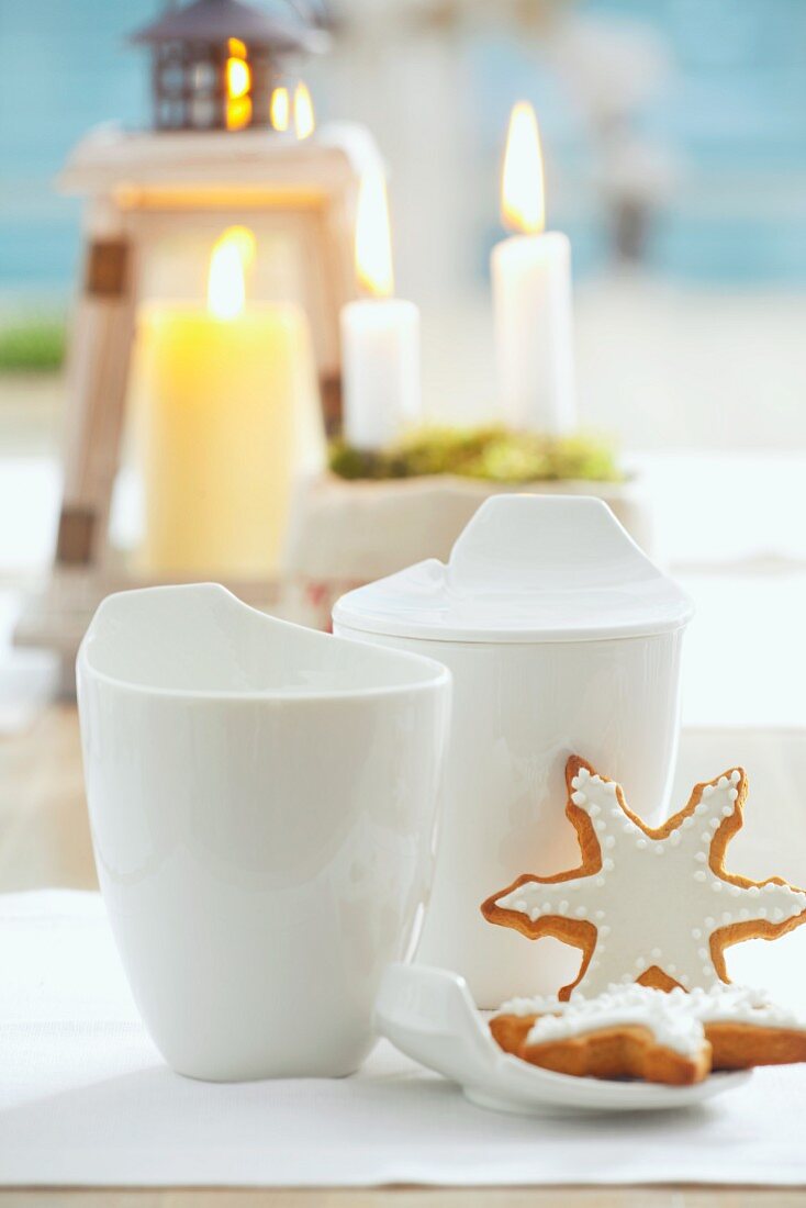 Lebkuchensterne mit Zuckerguss und weiße Tassen vor Kerzen