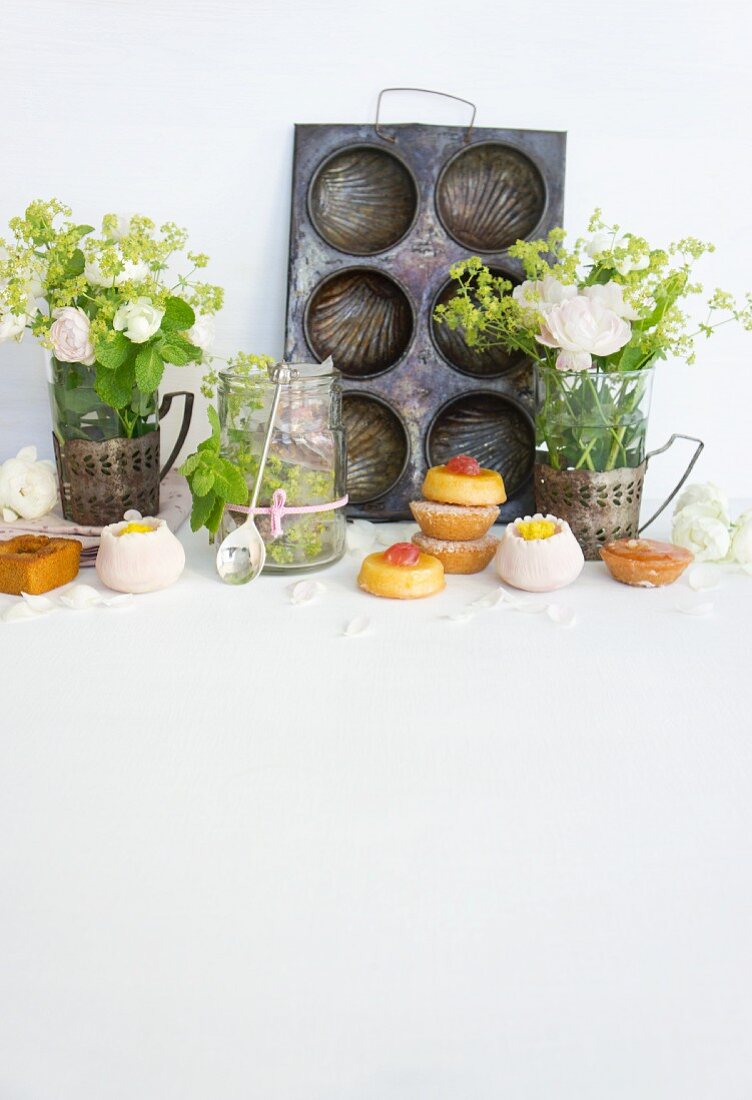 Mini cakes and confectionery in front of an old baking tray and vases of flowers