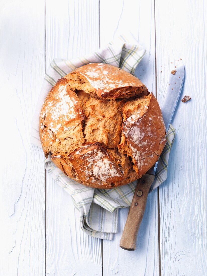 A rustic loaf on a tea towel with a bread knife