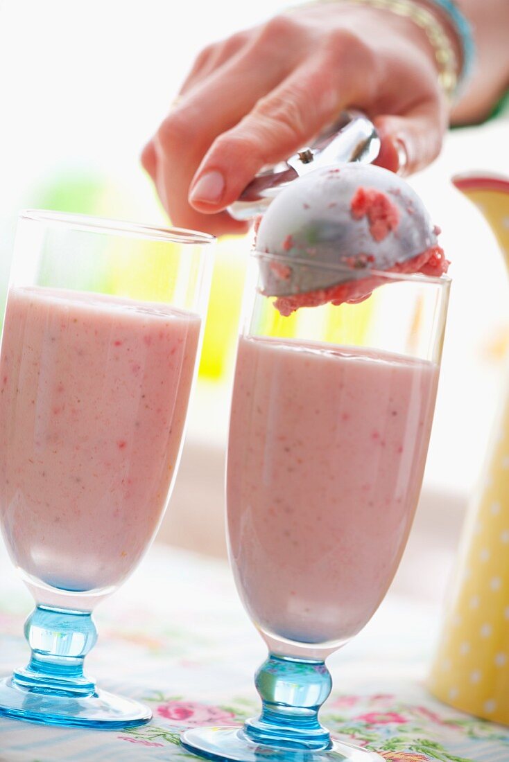 A scoop of strawberry ice cream being added to a milkshake