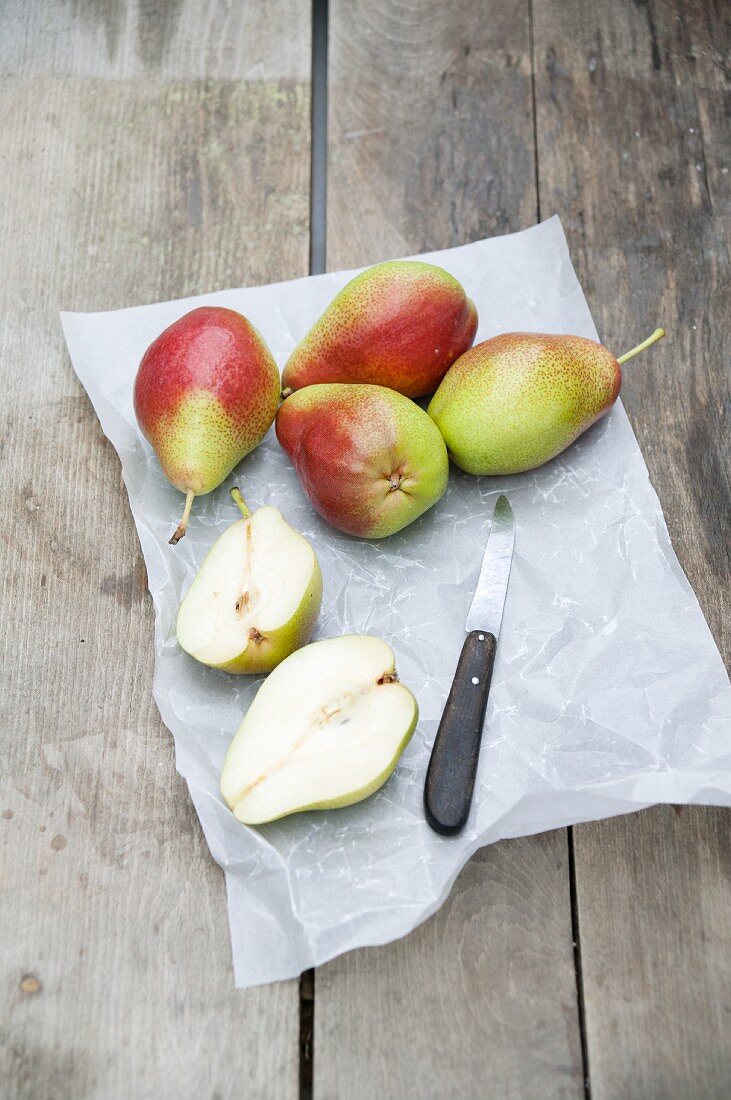 Several pears, whole and halved, on grease-proof paper with a knife
