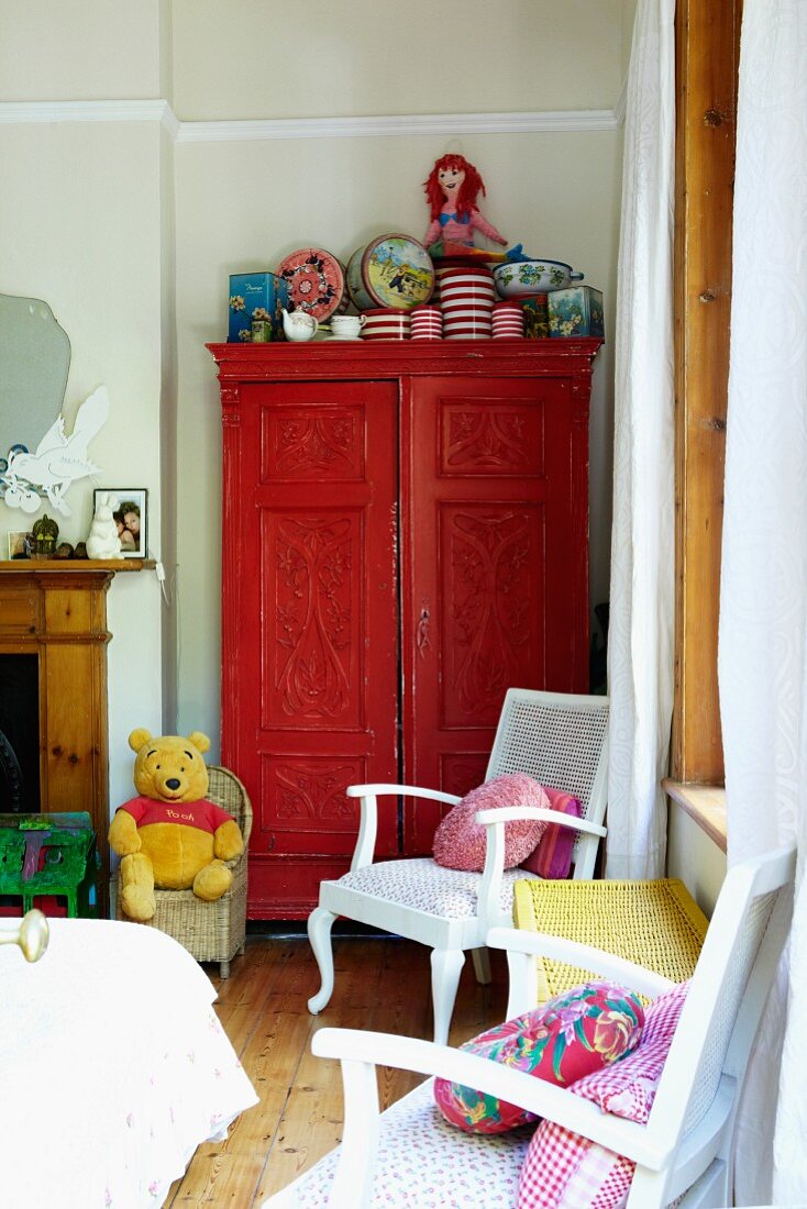 White chairs with colourful scatter cushions and red-painted cupboard in corner of child's bedroom