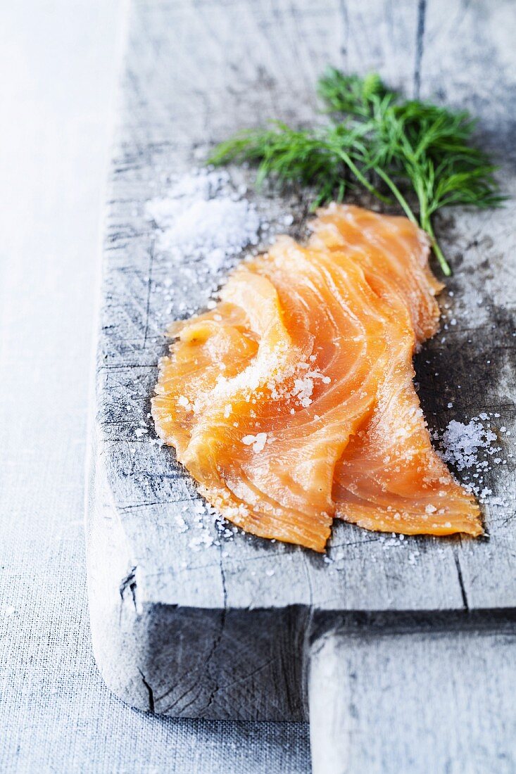Smoked salmon with dill and coarse sea salt on a rustic wooden board