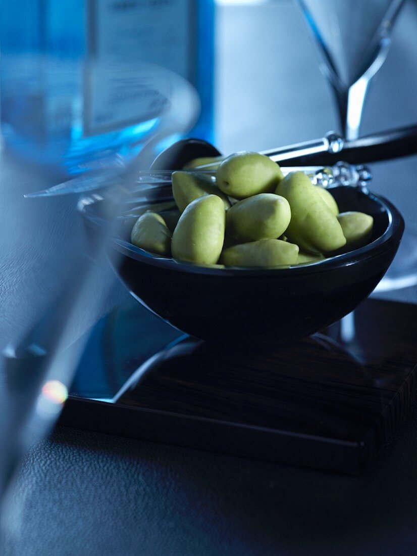 A bowl of green olives between martini glasses