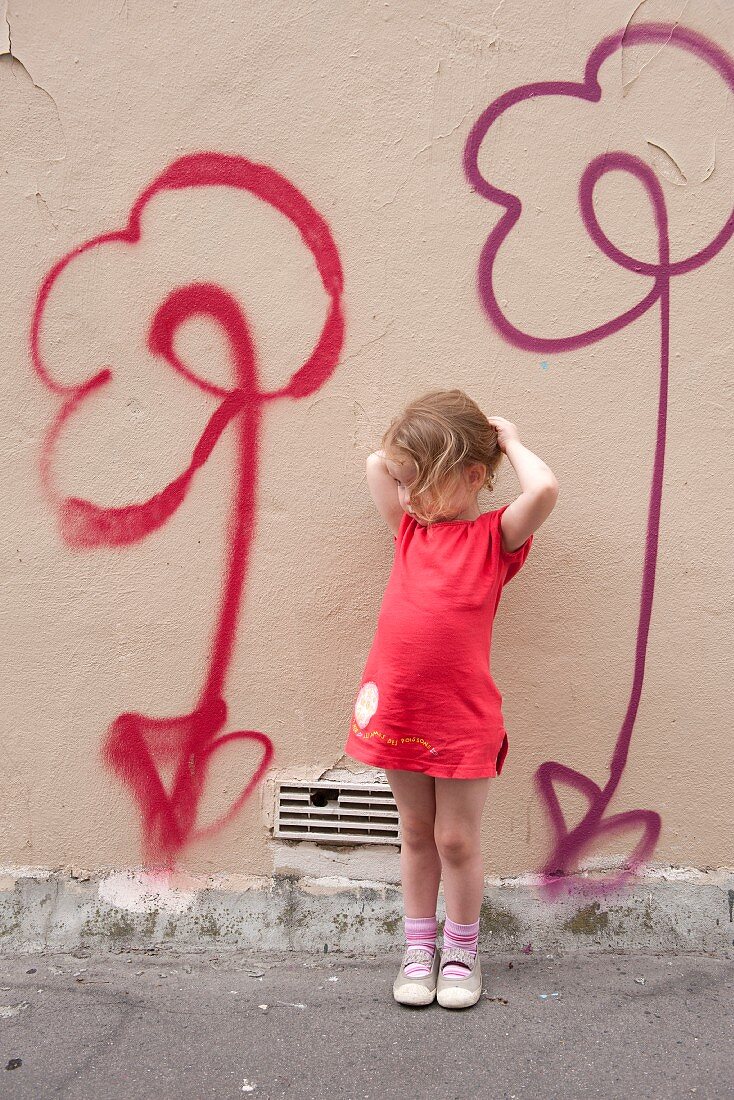 Little girl standing in front of flower motifs spray-painted on wall