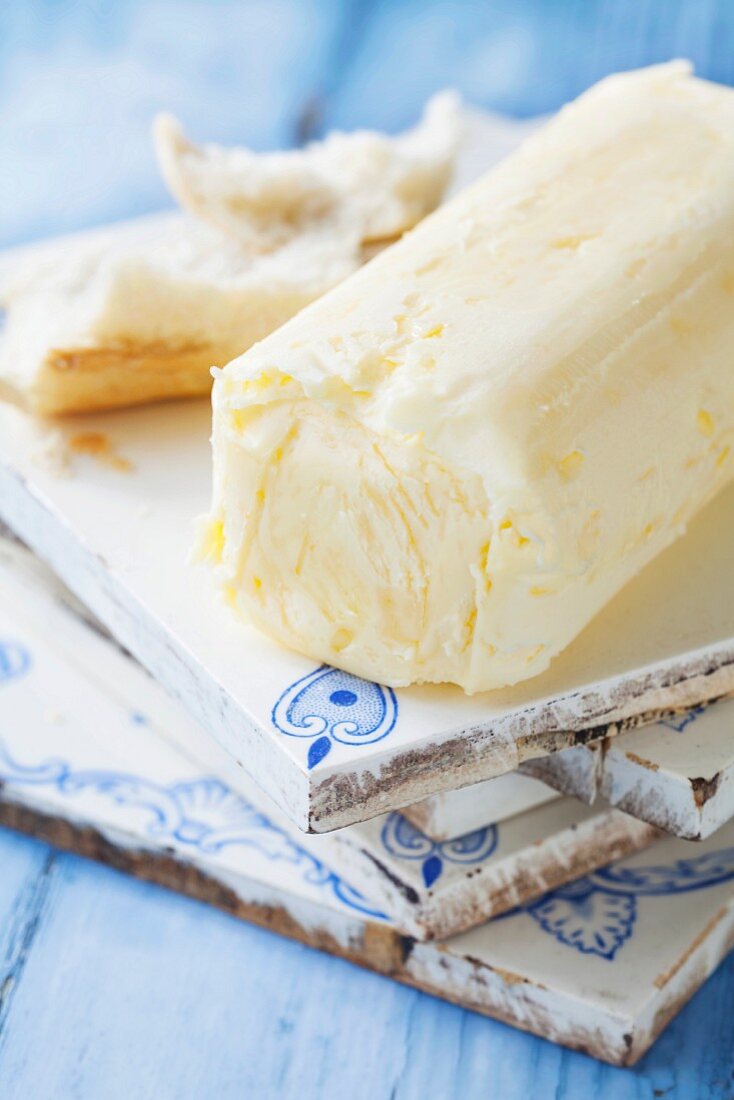 Ein Stück Meersalz-Butter in der Rolle mit Weißbrotstücken auf blau-weißem Hintergrund RM