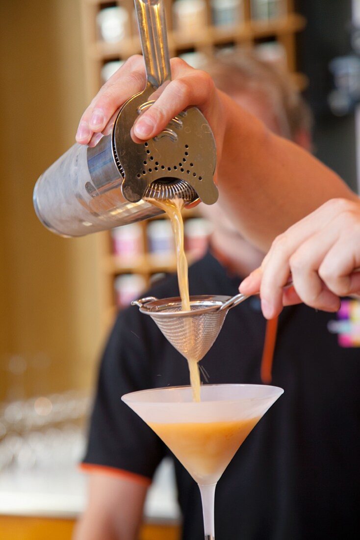 Mann schüttet Eistee aus dem Shaker in ein Cocktailglas