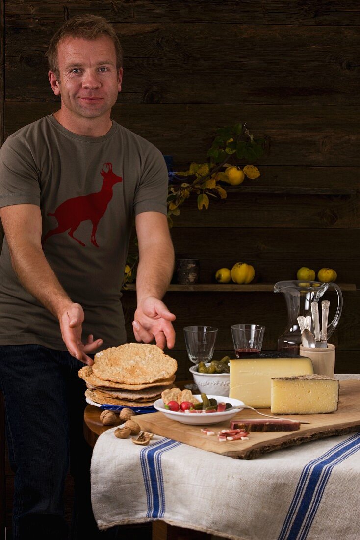 Mann serviert rustikale Südtiroler Brotzeit mit Rohschinken, Schüttelbrot, Nüssen, Käse und Wein
