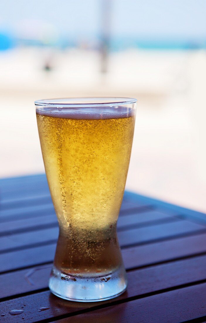 Glas kaltes Bier auf einem Tisch im Freien am Strand
