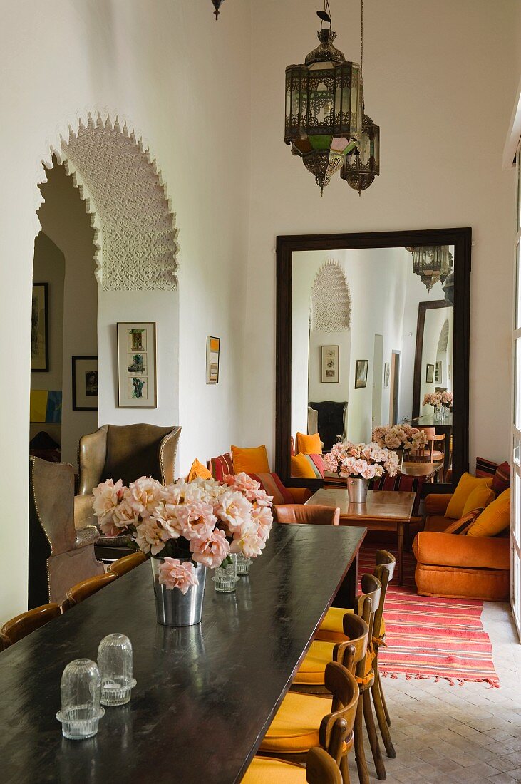 Moroccan lantern lamps above long dining table and seating area with large mirror in background