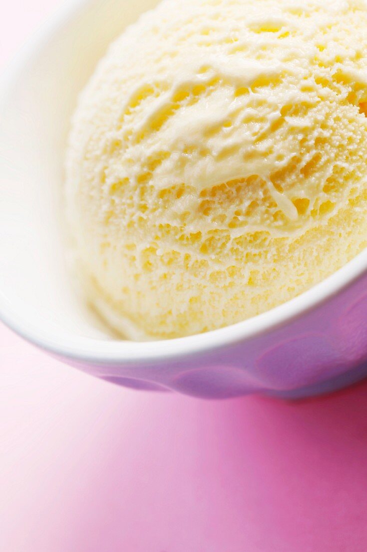 A scoop of vanilla ice cream in a bowl on a pink surface