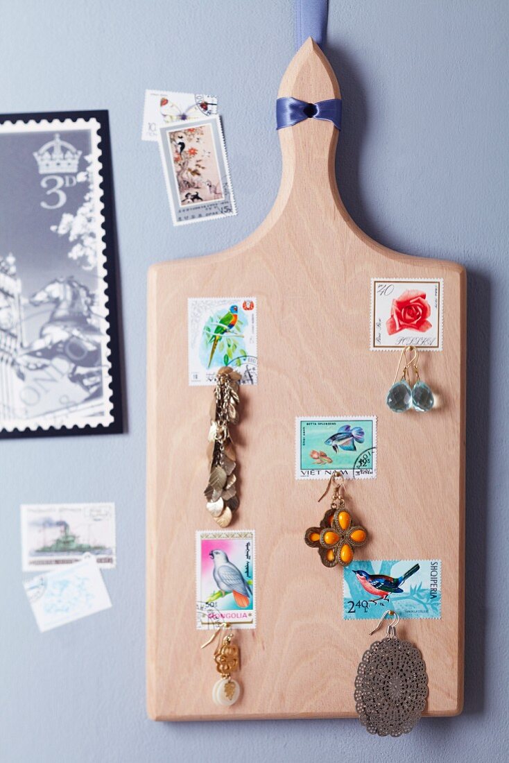 Chopping board decorated with postage stamps and used as a jewellery rack