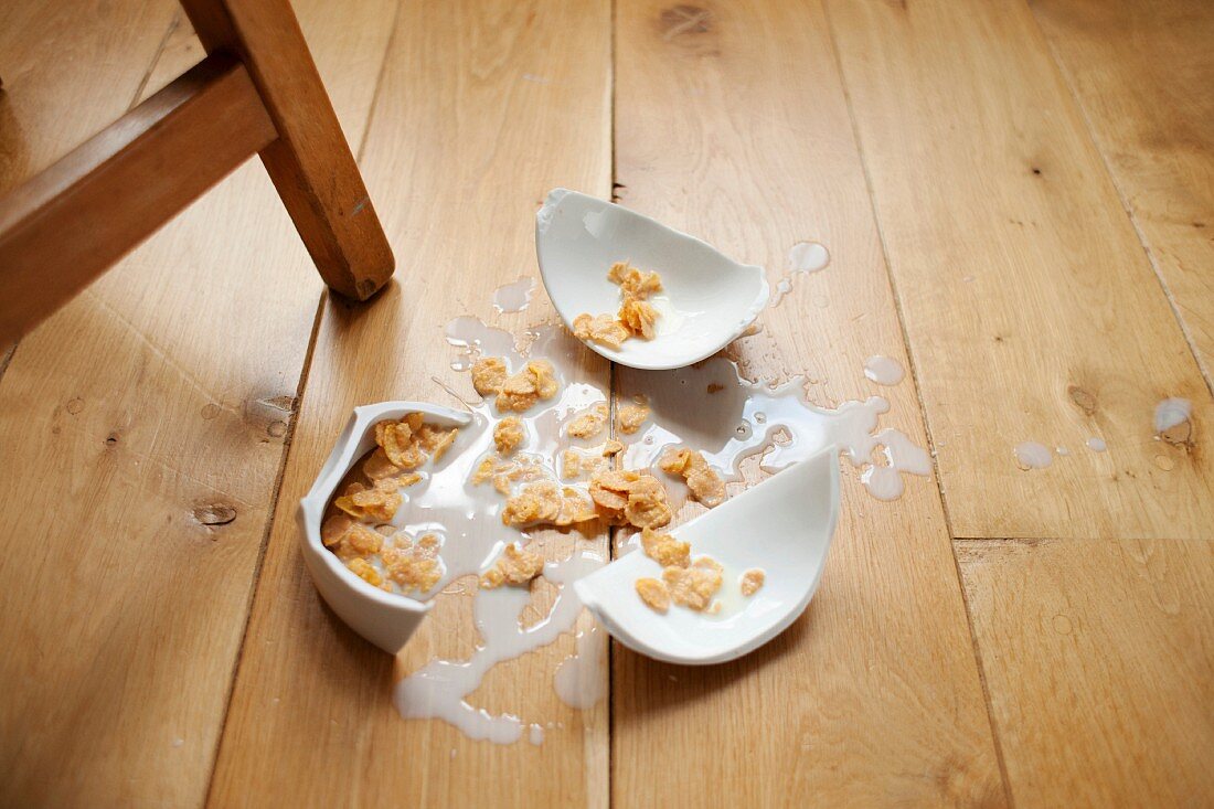 Broken bowl of cereal on wooden floor