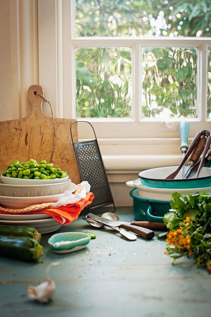 Küchenszene mit Gemüse, Geschirr, Besteck und Utensilien vor dem Fenster