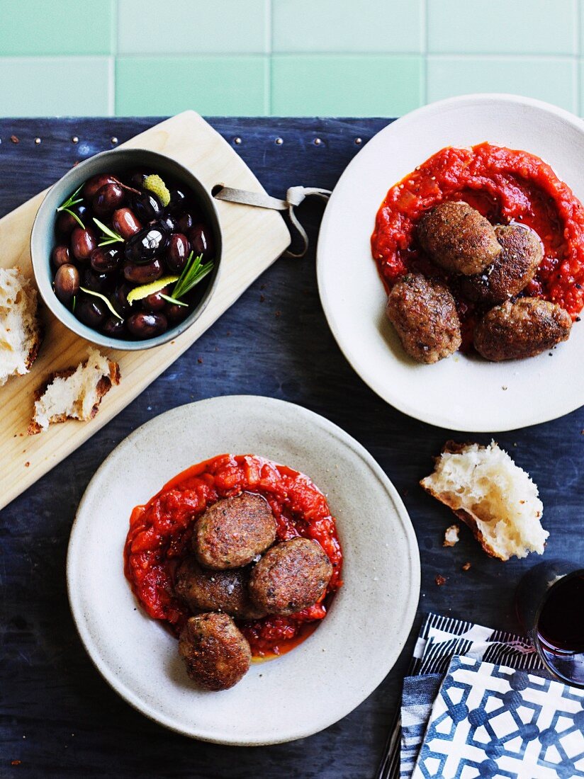 Mondeghili (meatballs from Milan) in tomato sauce with a dish of black olives