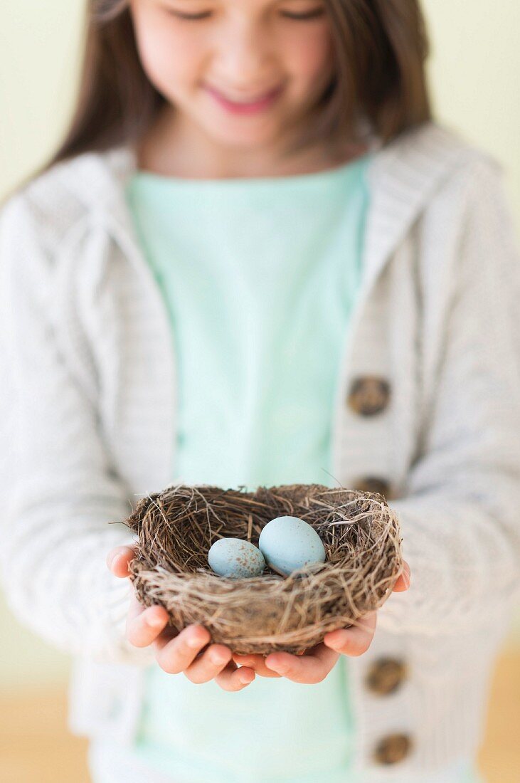 A girl holding a bird's nest with two bird's eggs in her hands