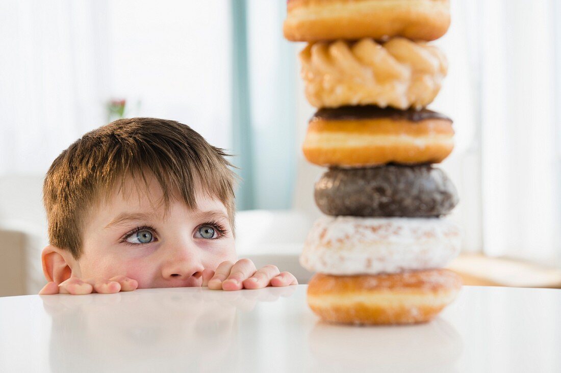 A small boy looking over the edge of a table at a stack of baked goods