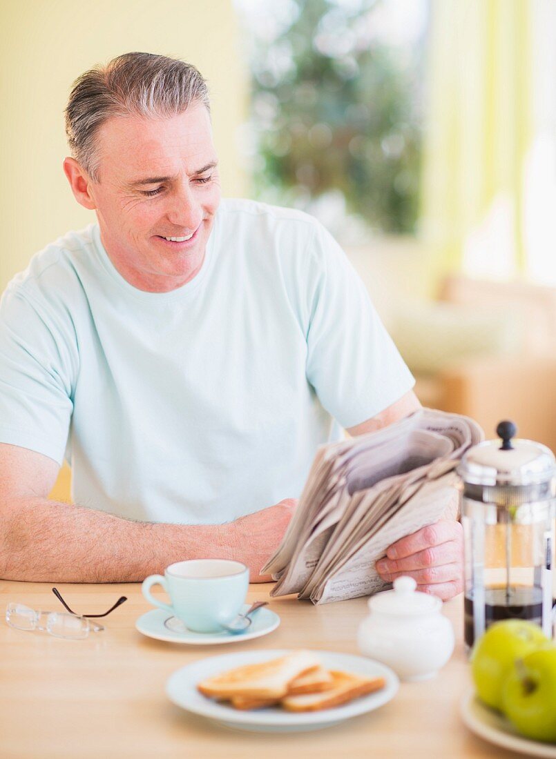Mann sitzt am Frühstückstisch und liest Zeitung