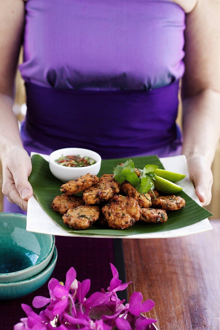A woman carrying a plate of Thai fishcakes