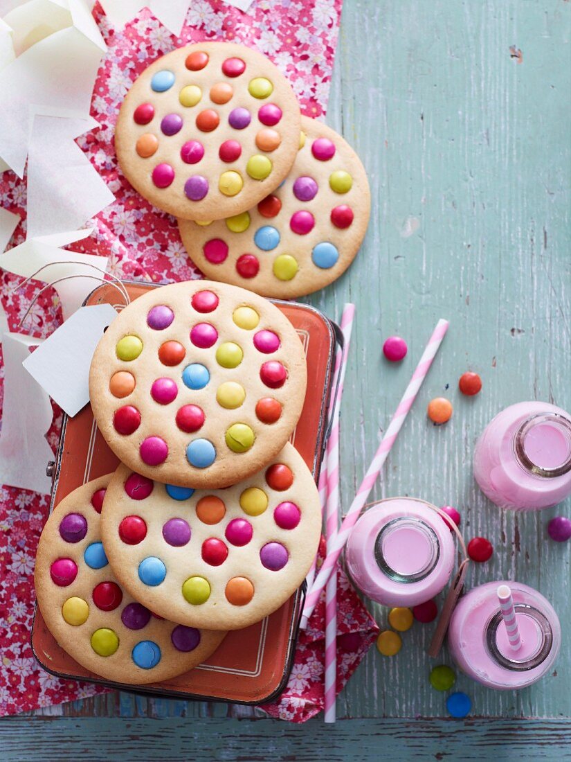 Giant cookies decorated with colourful chocolate beans and bottles of strawberry milkshake