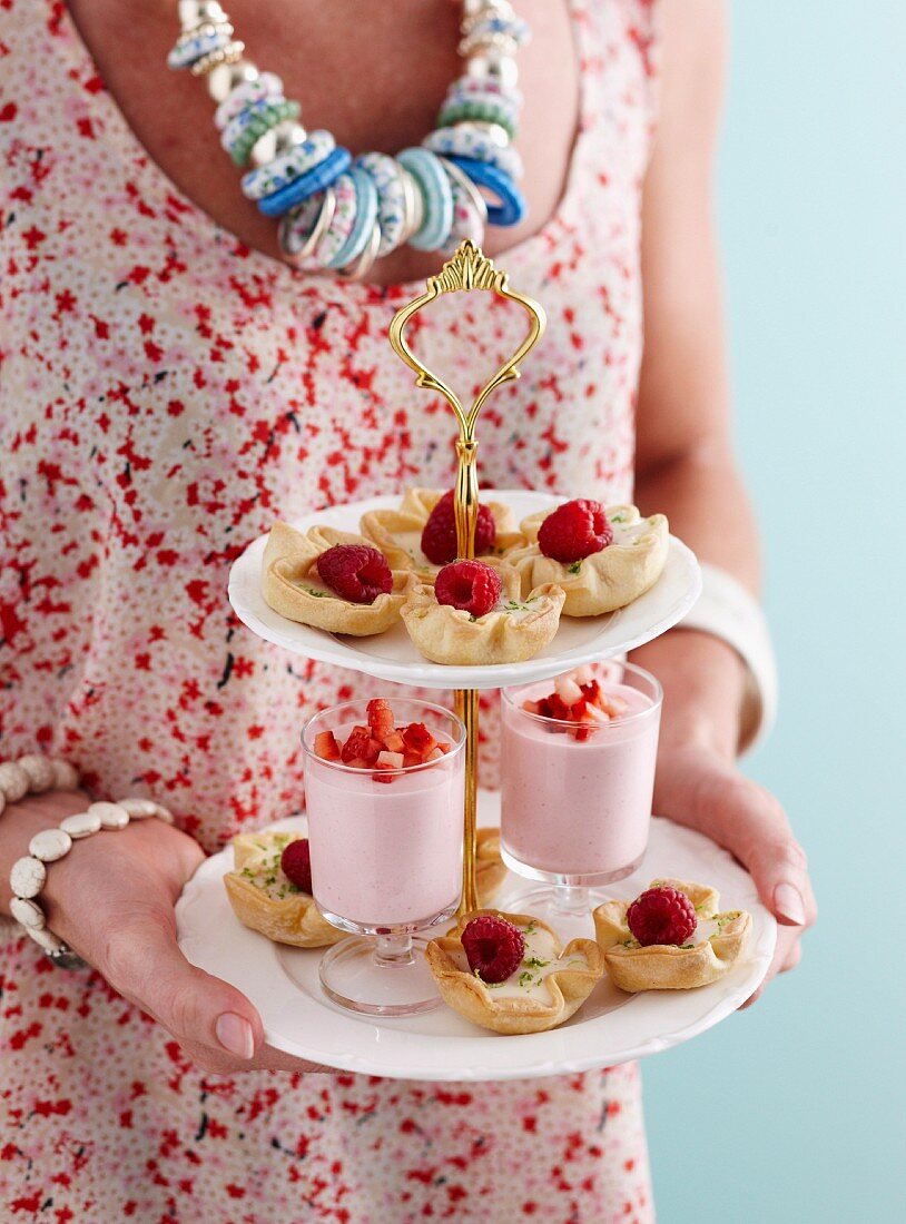 A woman holding a cake stand with panna cotta tartlets and strawberry mousse