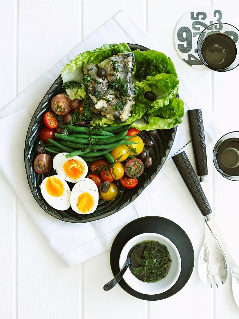 Salad nicoise on an oval platter with bowls of dressing