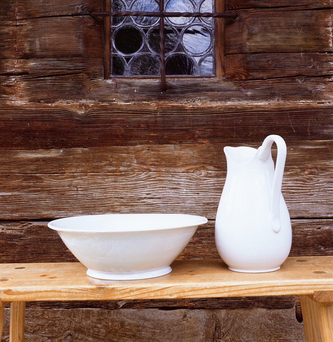 Hand-made pottery washbasin and jug on wooden bench against historical wooden facade