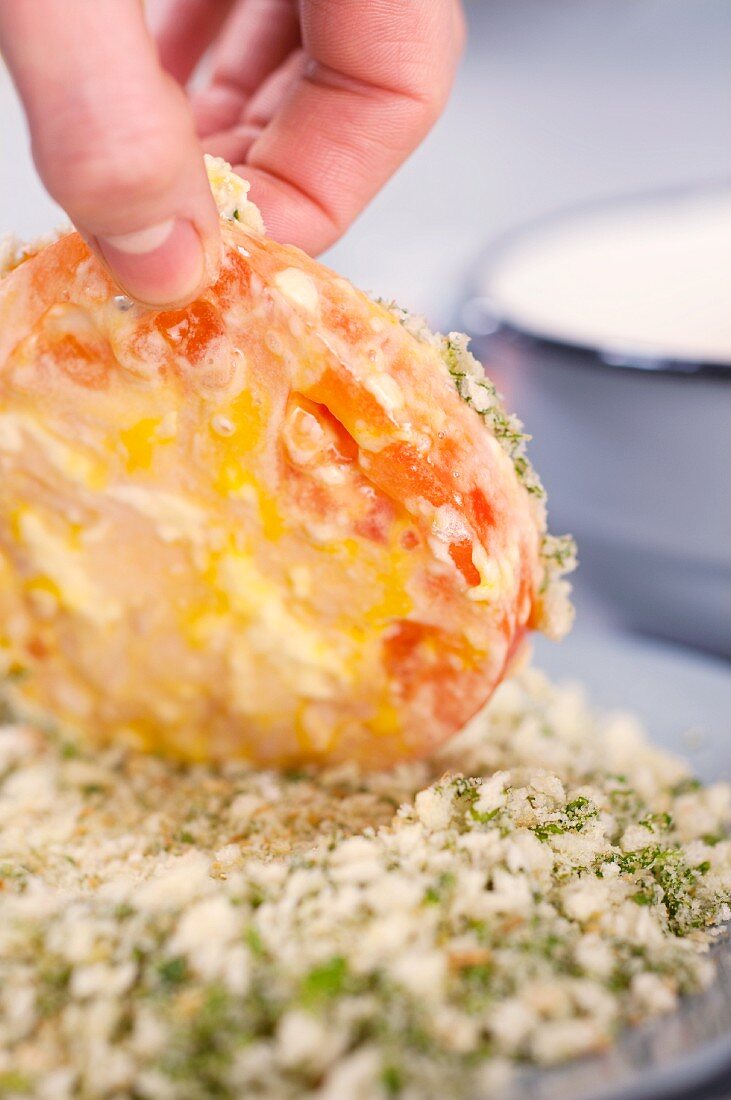 Tomato slices being coated in breadcrumbs