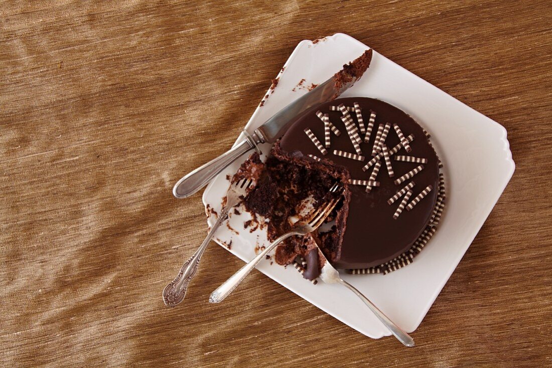 Schokoladenkuchen auf einem Kuchenteller, teilweise mit Gabeln gegessen und ein Messer
