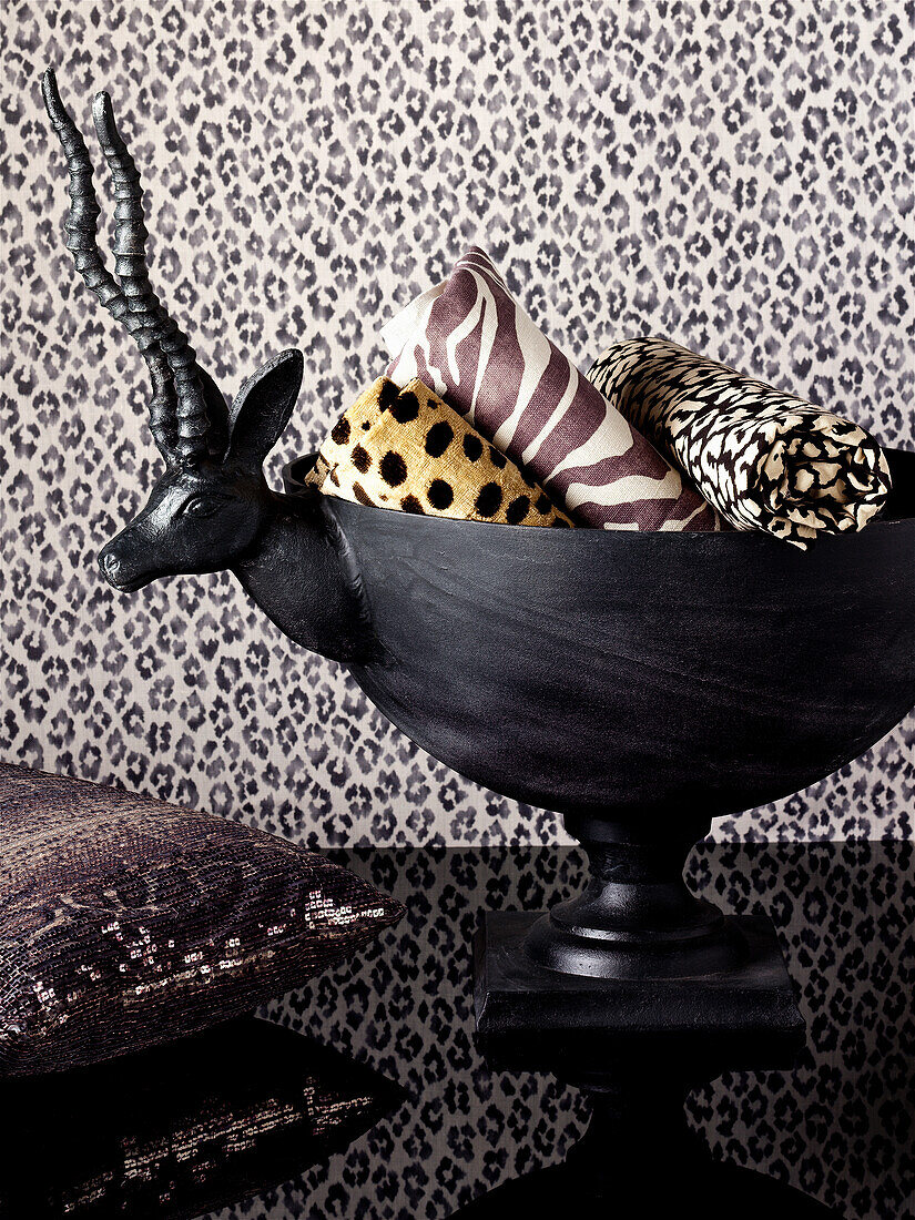 Rolls of fabric in animal-skin prints in bowl with antelope head