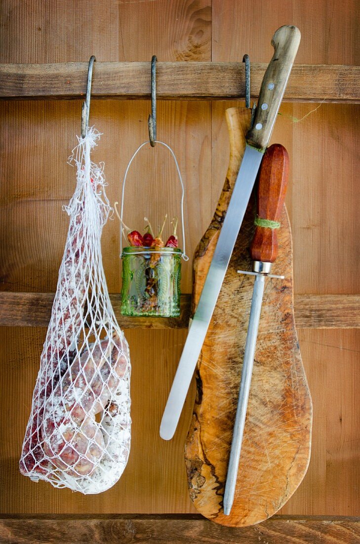 Netz mit verschiedenen Salamisorten, Chilischoten, Messer und Brett