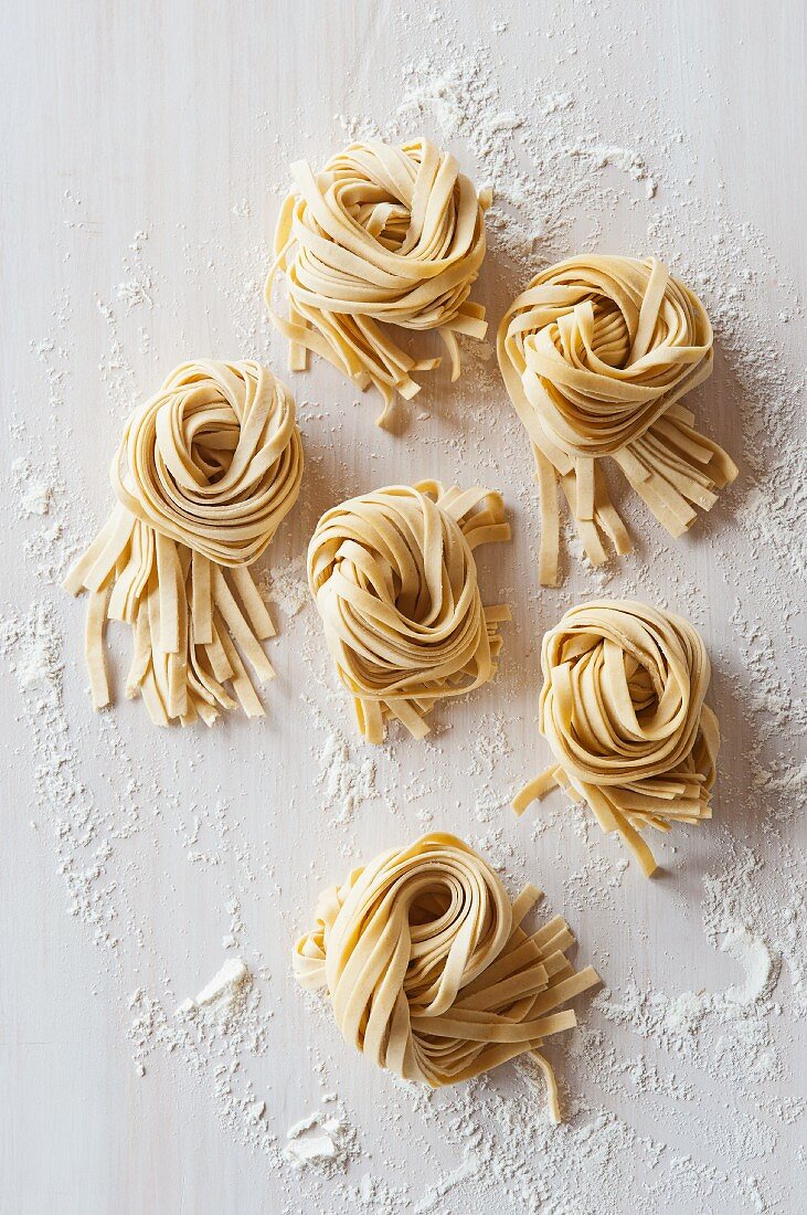 Nests of flat noodles on a floured worktop (view from above)