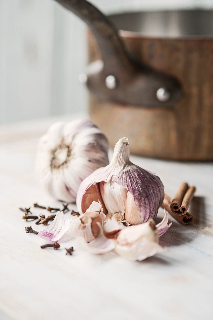 A still life featuring garlic, cloves and cinnamon sticks