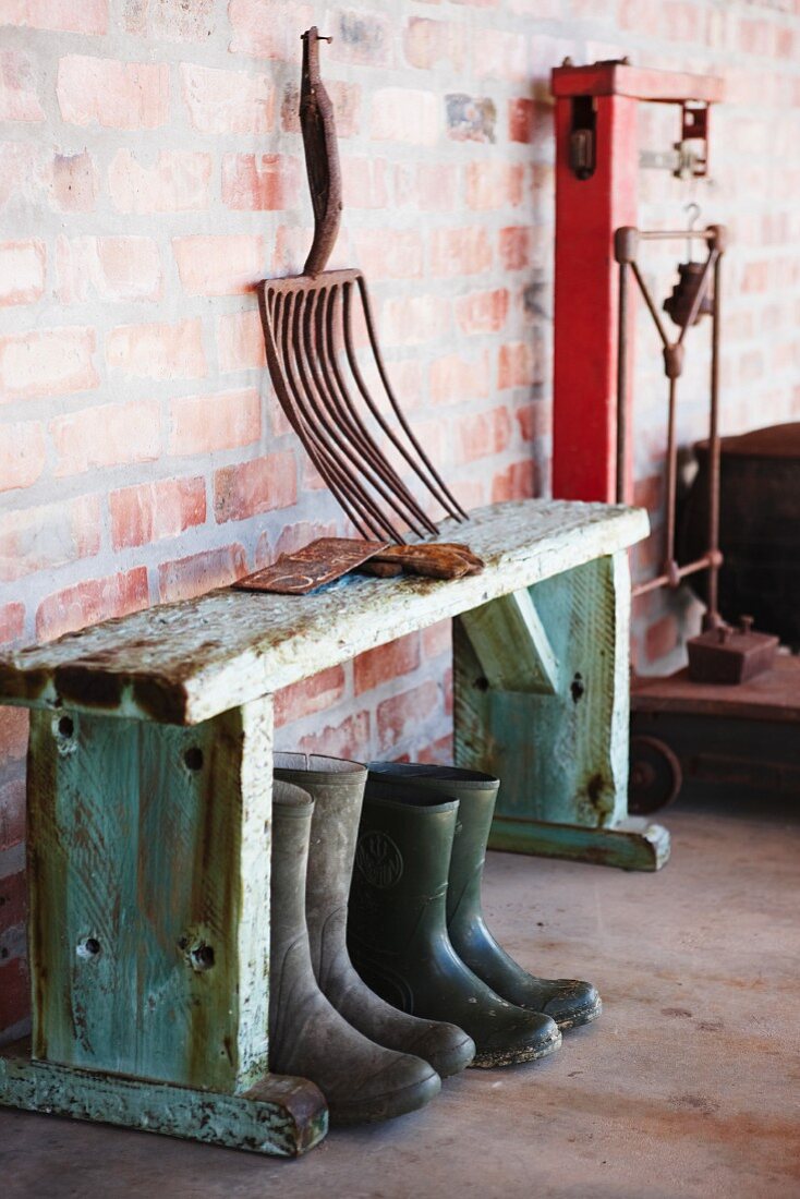 Vintage gardening tool on rustic wooden bench over wellington boots against brick wall