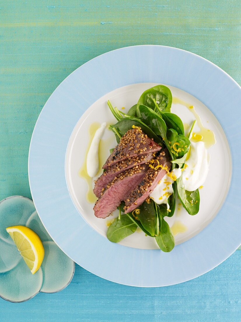 Marinated lamb fillet with mustard seeds on spinach leaves