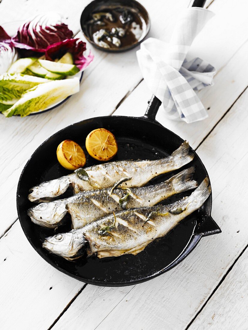 Three panfried whole bass, served in a cast-iron pan