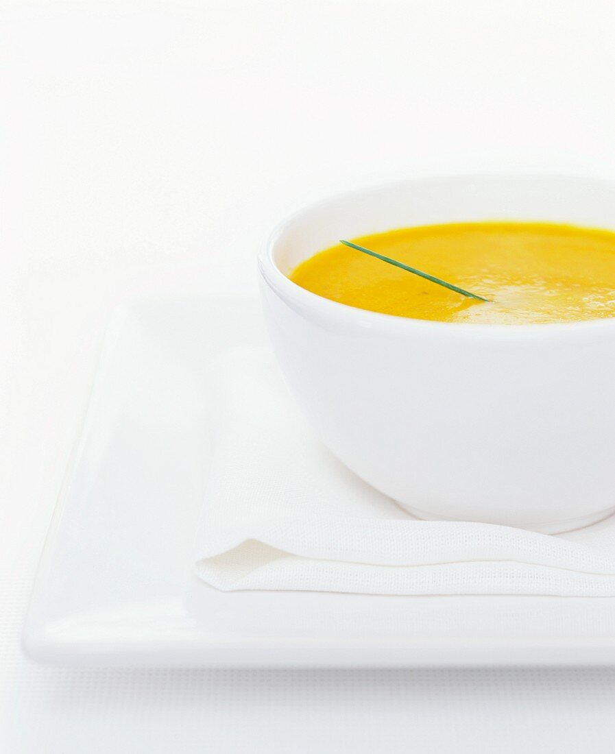A white bowl of carrot soup with a single chive garnish